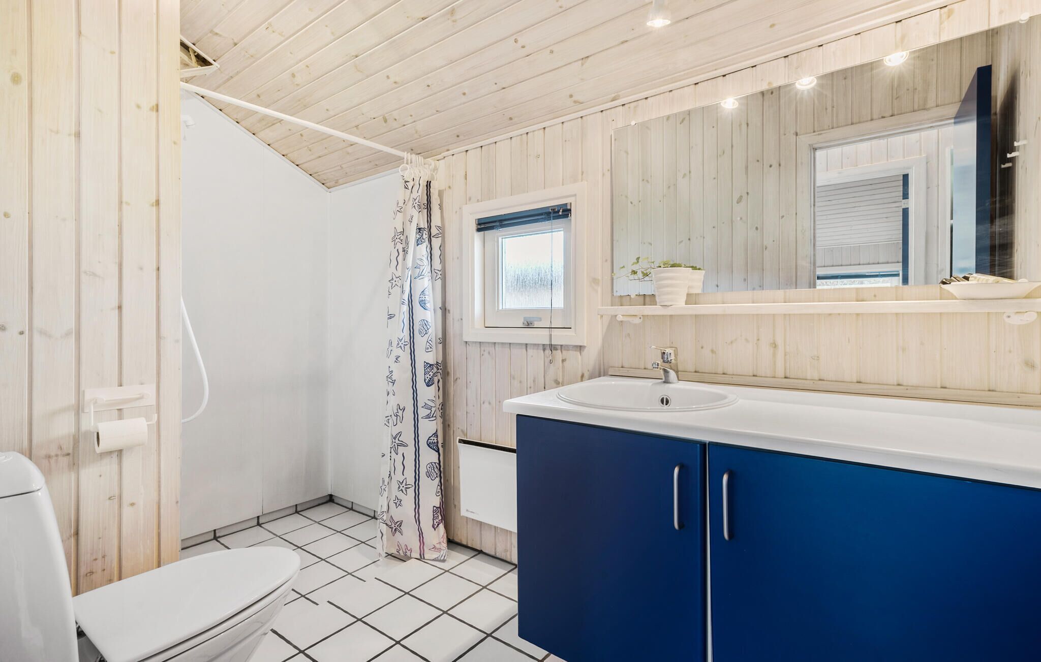 Un ba ño con inodoro, lavamanos y cortina de ducha con estampado de estrellas de mar.