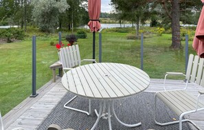Una mesa redonda con patas de metal, rodeada de sillas blancas, sobre una terraza de madera con un tapete gris.