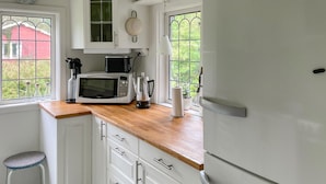 A compact kitchen with white cabinets, a wooden countertop, a microwave, a kettle, and a refrigerator.
