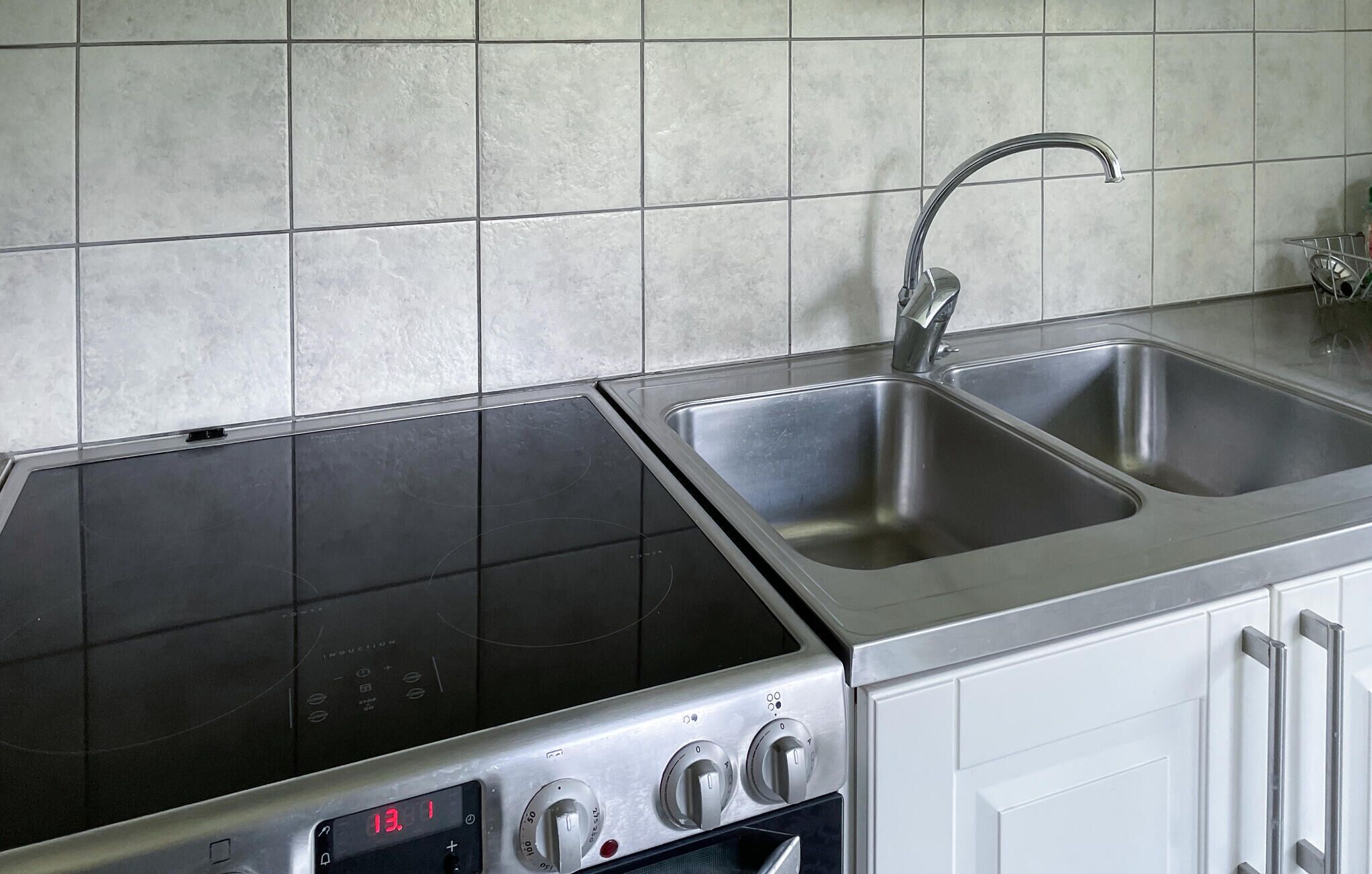 A kitchen with a stainless steel sink, a built-in stovetop, and white cabinetry.