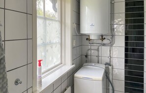 Un baño con ventana, calentador de agua y lavadora.