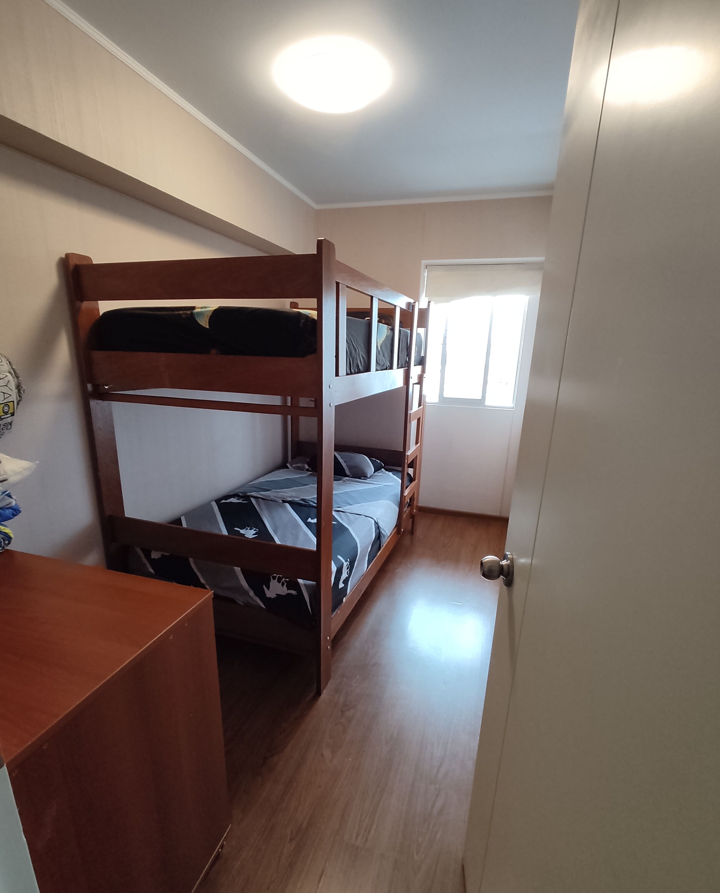 A bunk bed room with a wooden desk and a wardrobe.