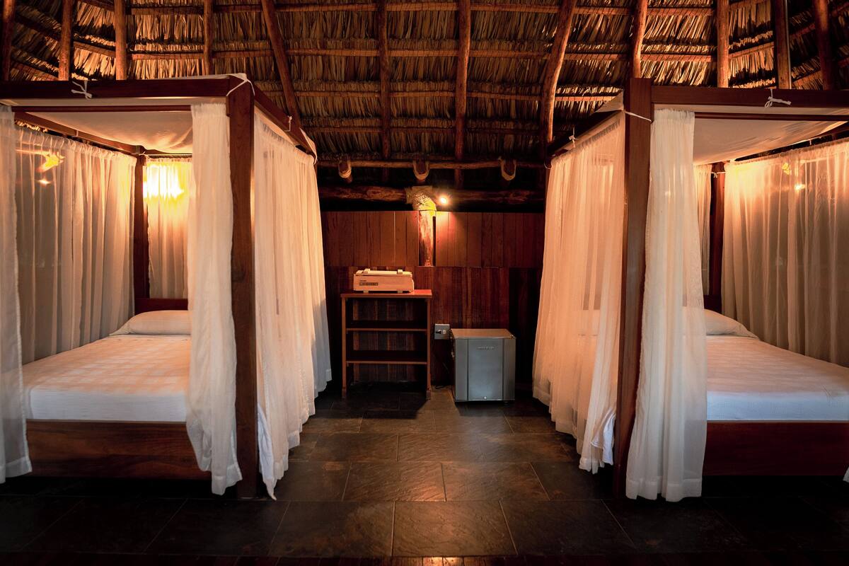 A room with two beds, each with a canopy, a small table, and a shelf with items.