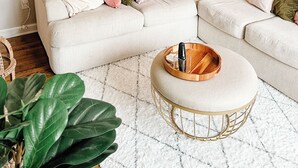 Una sala de estar con un sofá seccional, una mesa de centro redonda y una planta en maceta.