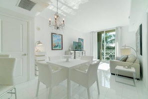 Uma sala de estar clara e moderna com uma área de jantar branca, um candelabro e uma varanda com vista.