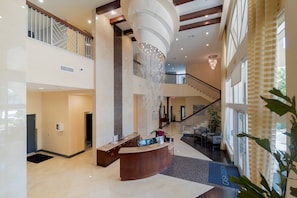 Um hall amplo com balcão de recepção, um candelabro e uma escadaria para um andar superior.