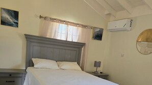 Une chambre à coucher comprenant un lit, des tables de chevet, une commode et un climatiseur fixé au mur.