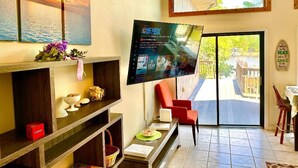 Een woonkamer met een flatscreen televisie, een rode stoel, een eettafel en uitzicht op buiten.