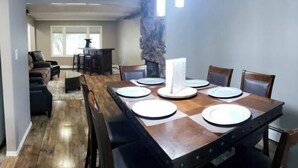 Un comedor con una mesa de madera dispuesta para seis personas, una pared de acento de piedra y vistas a una sala de estar con chimenea.