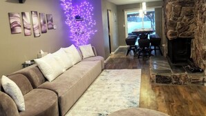 A living room with a sofa, a fireplace, a dining area, and a wall with purple lights.