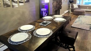 A dining area with a long wooden table set for four, surrounded by modern decor and a large rock feature.