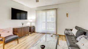 Een moderne woonkamer met een glazen salontafel, een bank, een houten kast en een plafondventilator.