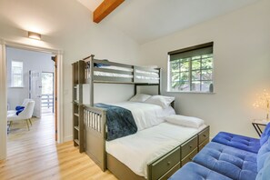 Un dormitorio con una cama litera, una cama individual, un sofá azul y una ventana con vistas a la vegetación.