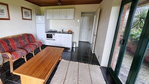 A compact living space with a sofa, a wooden table, a kitchen area, and a sliding glass door leading to an outdoor area.