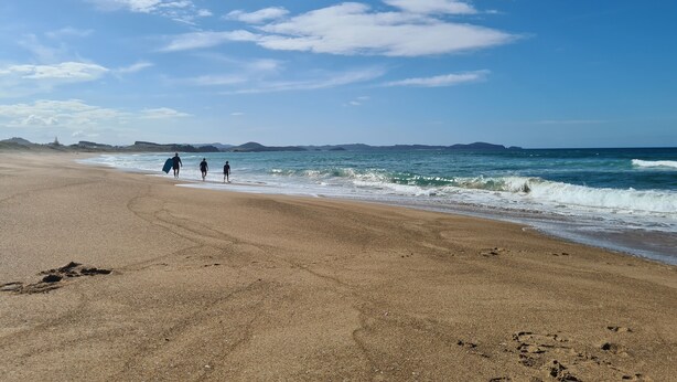 A beach with a clear sky, calm sea, and distant hills.