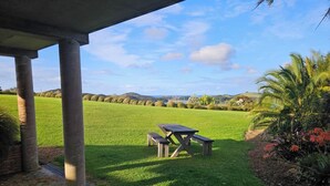 A picnic table under a covered area with a view of a grassy field and distant hills.