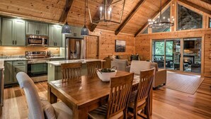 A spacious log cabin interior with a wooden dining table, chairs, a kitchen area, and a cozy living space with a fireplace. - The Retreat at Laurel Creek- Screened Porch, Hot Tub, Outdoor Fireplace (Blue Ridge)