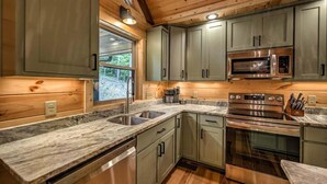 A modern kitchen with granite countertops, stainless steel appliances, and wooden cabinetry. - The Retreat at Laurel Creek- Screened Porch, Hot Tub, Outdoor Fireplace (Blue Ridge)