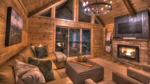 A cozy log cabin interior with a large wooden ceiling, a fireplace, a comfortable seating area, and a television mounted on the wall. - The Retreat at Laurel Creek- Screened Porch, Hot Tub, Outdoor Fireplace (Blue Ridge)