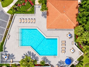 Vista aérea de un área de piscina con techo de azulejos, sillas de descanso y un jardín ajardinado.