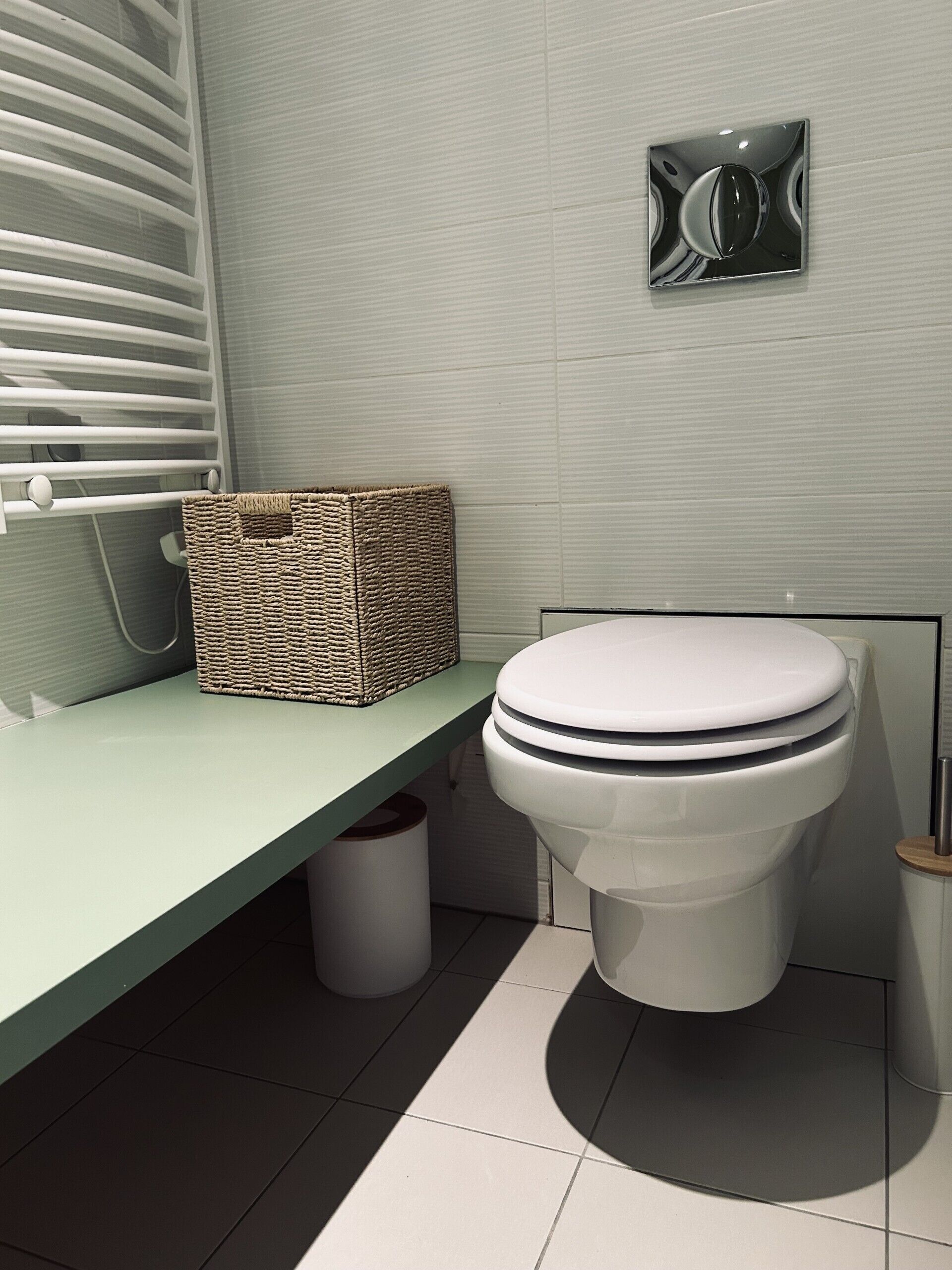 Un baño con inodoro, una cesta de mimbre en un estante y una lámpara de pared.