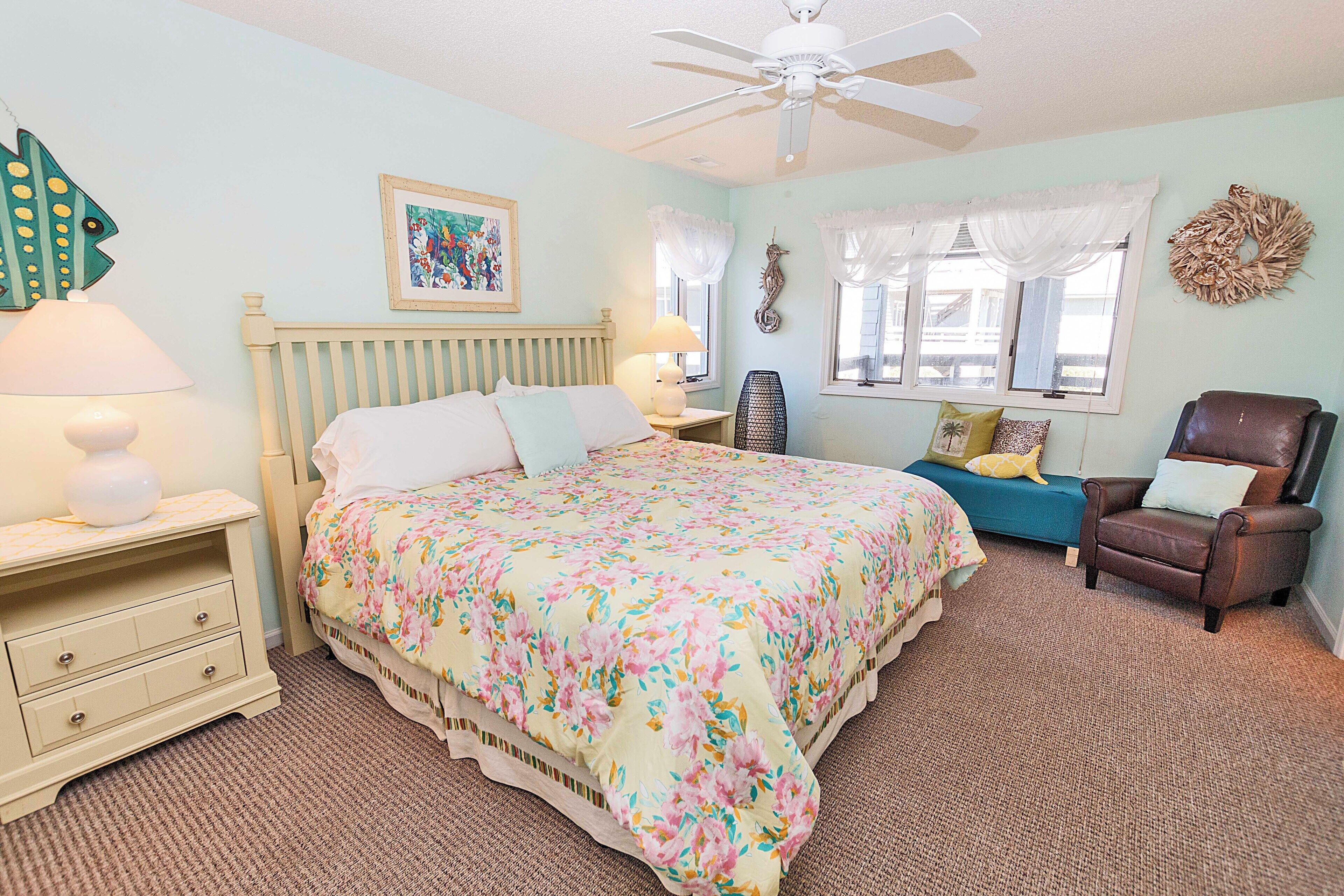 A bedroom with a bed, nightstands, a chair, a ceiling fan, and a window with curtains.