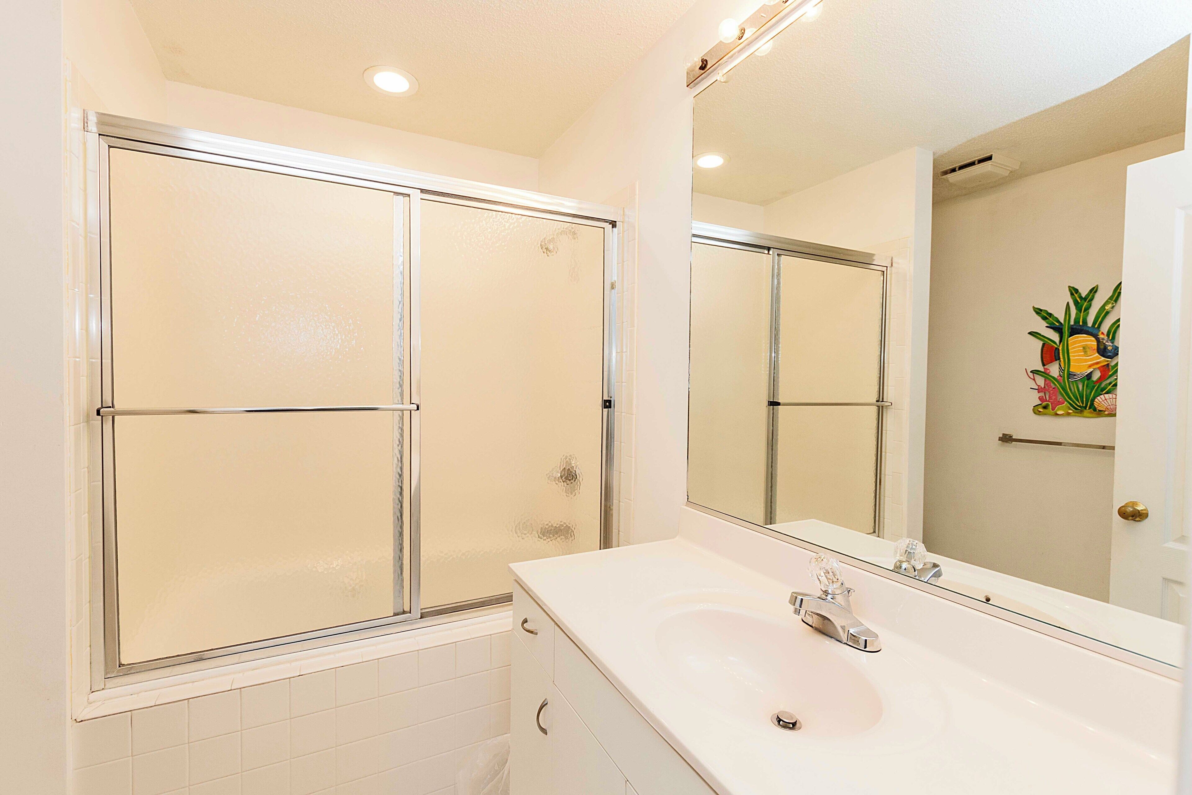 A bathroom with a glass-enclosed shower, a white sink, and a large mirror.