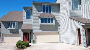 Ein zweistöckiges Wohnhaus mit Garage, einer roten Tür und einem kleinen Vorgarten mit einem Busch.