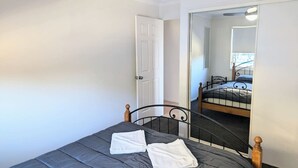 A bedroom with a single bed, a ceiling fan, and a door leading to another room. - Burleigh Breeze Coastal (Burleigh Heads)
