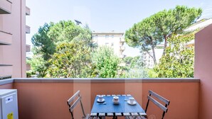 A balcony with a table and chairs, overlooking a residential area with trees and buildings.