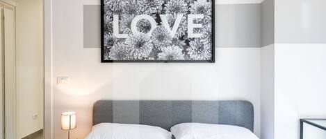 A bedroom with a bed, white pillows, a bedside lamp, and a framed picture on the wall.