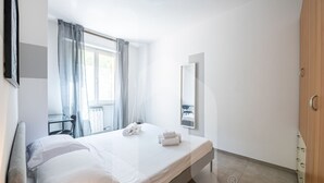 A hotel room with a bed, a desk, a chair, a mirror, and a wardrobe.
