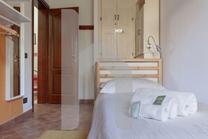Una habitación de hotel con cama, cabecero de madera, mesita de noche con lámpara y armario.