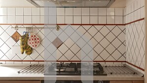 Une cuisine aux murs recouverts de carreaux blancs, avec une cuisinière à gaz et des ustensiles de cuisine suspendus.