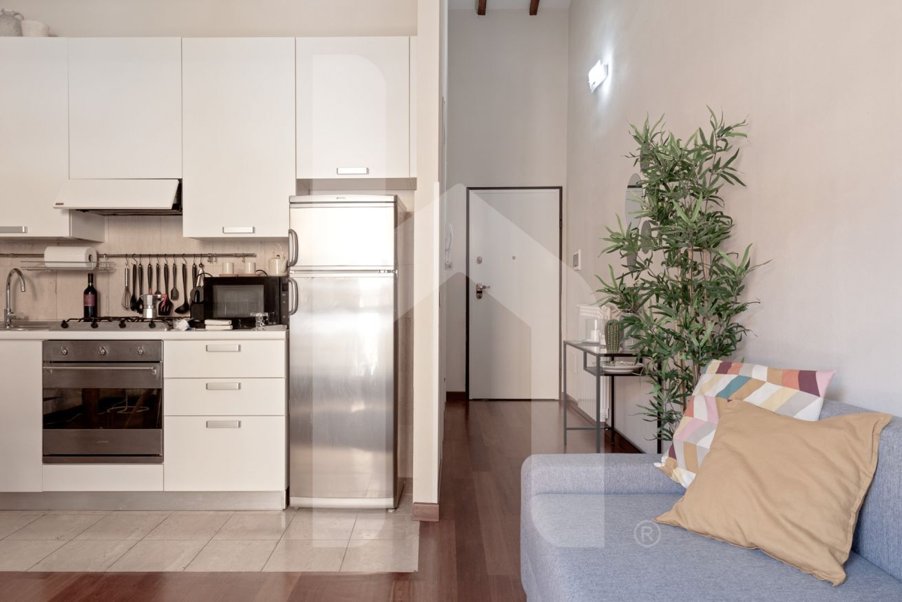 A modern kitchen with white cabinets, stainless steel appliances, and a blue sofa with a beige pillow.
