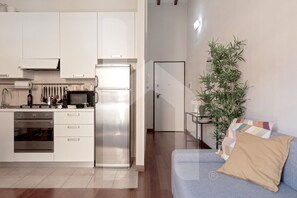 A modern kitchen with white cabinets, stainless steel appliances, and a blue sofa with a beige pillow.