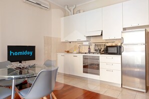 A modern kitchen with white cabinets, stainless steel appliances, and a glass dining table with chairs.