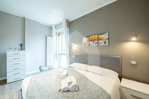 A modern bedroom with a large bed, a bedside table, a dresser, and a window with curtains.