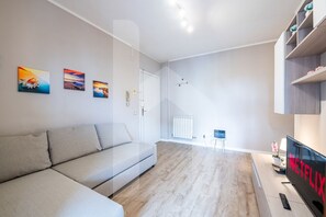 A modern living room with a grey sofa, a flat-screen TV, and a bookshelf.