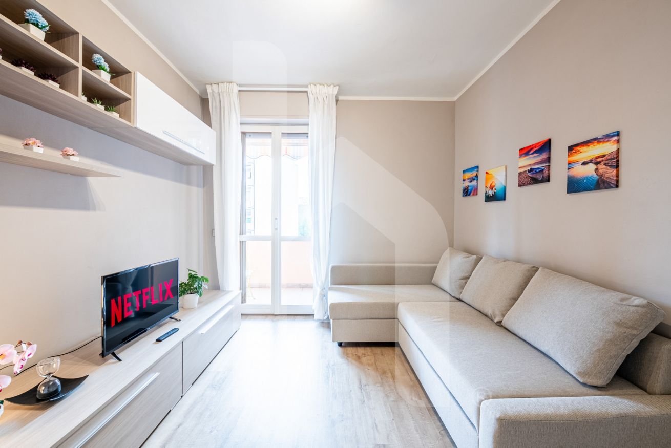 A modern living room with a sofa, a TV displaying 'NETFLIX', a window with curtains, and wall art.