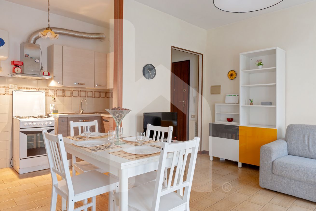 A modern kitchen with white cabinetry, a dining table set for four, and a sofa in the living area.