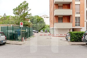 Une entrée fermée par un portail donnant sur un immeuble résidentiel, avec un panneau de signalisation indiquant un arrêt obligatoire, une clôture verte et des voitures garées.