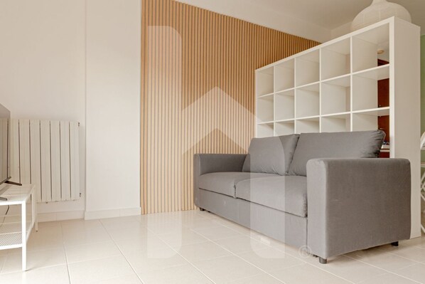 Un salon moderne avec un canapé gris, une étagère blanche et un radiateur blanc.