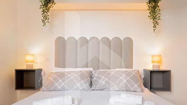 Ein ordentlich bezogenes Bett mit weißen Leinentüchern und zwei Kissen, begleitet von Nachttischen mit Lampen und Kerzen, in einem Zimmer im schlichten, modernen Stil.