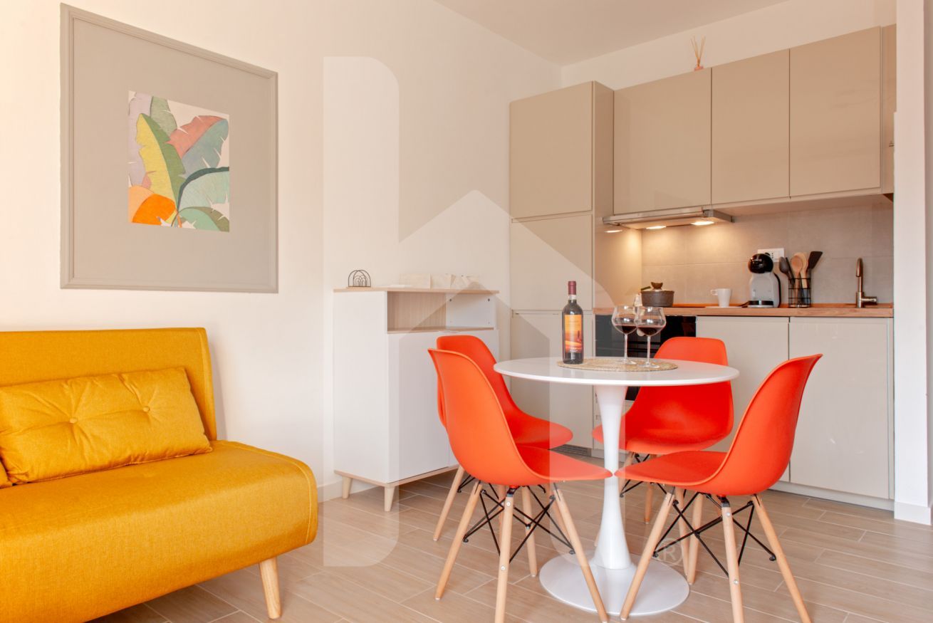 A modern kitchen with a dining table, orange chairs, and a sofa.