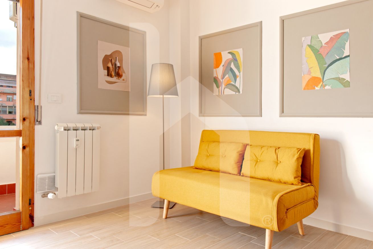 Un salon moderne avec un canapé jaune, des œuvres d’art encadrées accrochées aux murs, une lampe sur pied et un radiateur.