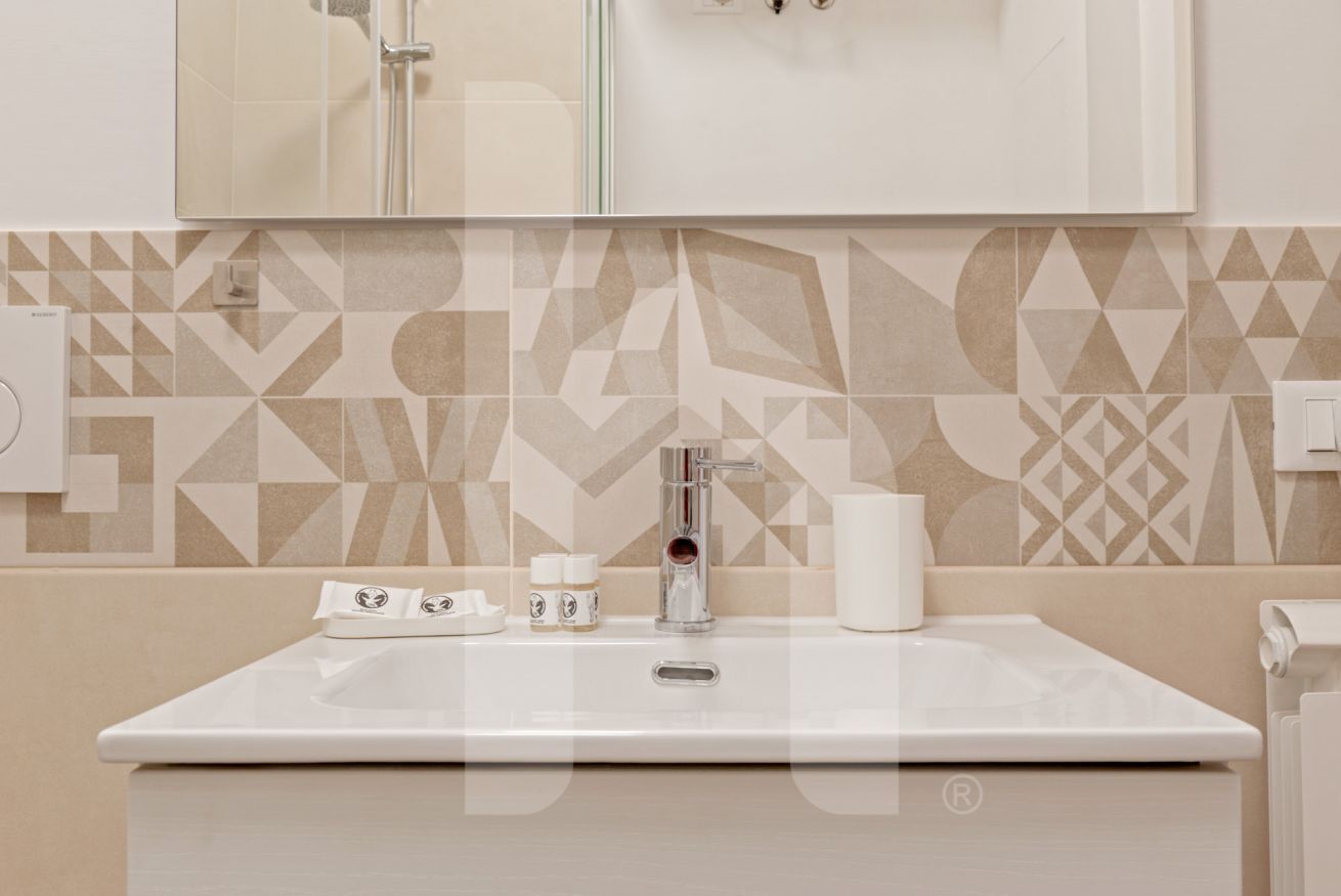 A bathroom with a white sink, a mirror above it, and a geometric patterned wall.