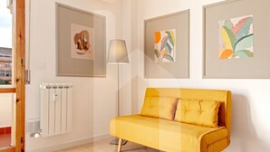 Ein modernes Wohnzimmer mit einem gelben Sofa, gerahmten Kunstwerken an den Wänden, einer Stehlampe und einer Heizung.