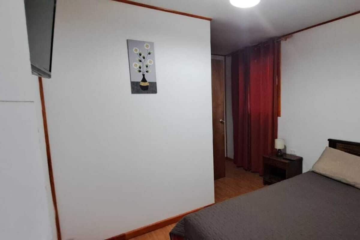 Een slaapkamer met een bed, een nachtkastje, een inbouwschakelaar en een deur met gordijn.
