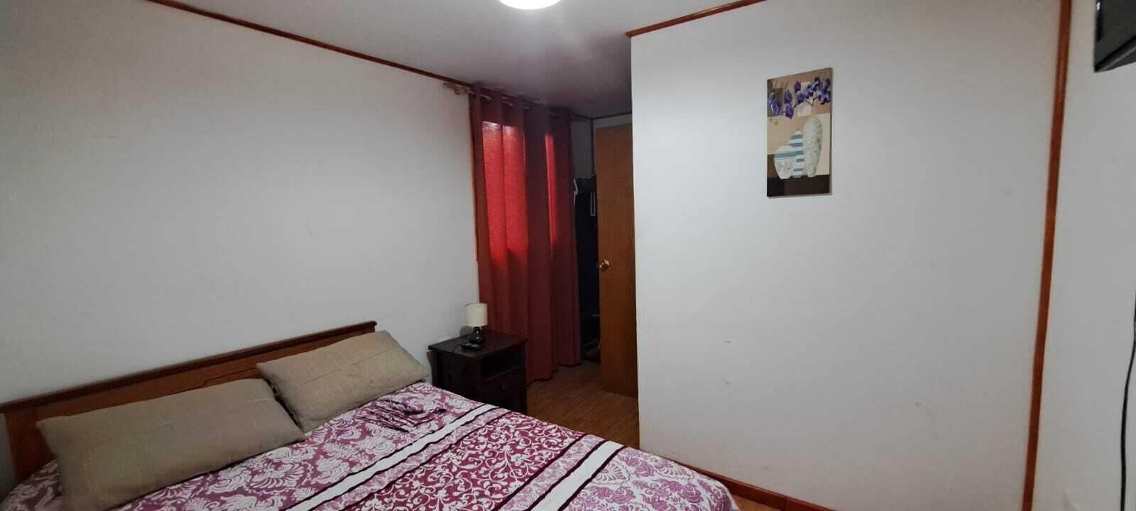 A bedroom with a bed, a nightstand, a lamp, a door, and a wall with a picture.